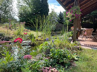 Neben einer einladenden Terrasse befindet sich ein von vielen Blumen umrahmter Naturteich., Foto: Sarah Mamerow, Lizenz: Naturpark Dahme-Heideseen